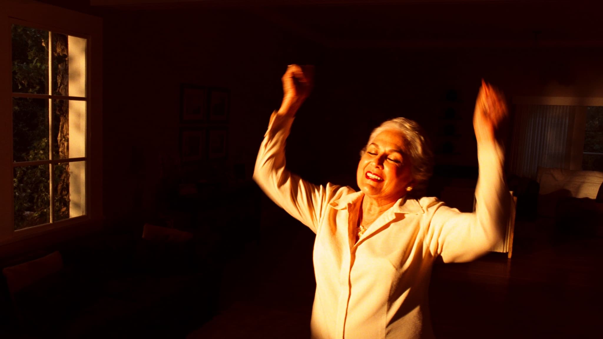 Anciana latina bailando con sonrisa de alegría en su sala con luz dorada del atardecer, vitalidad digna