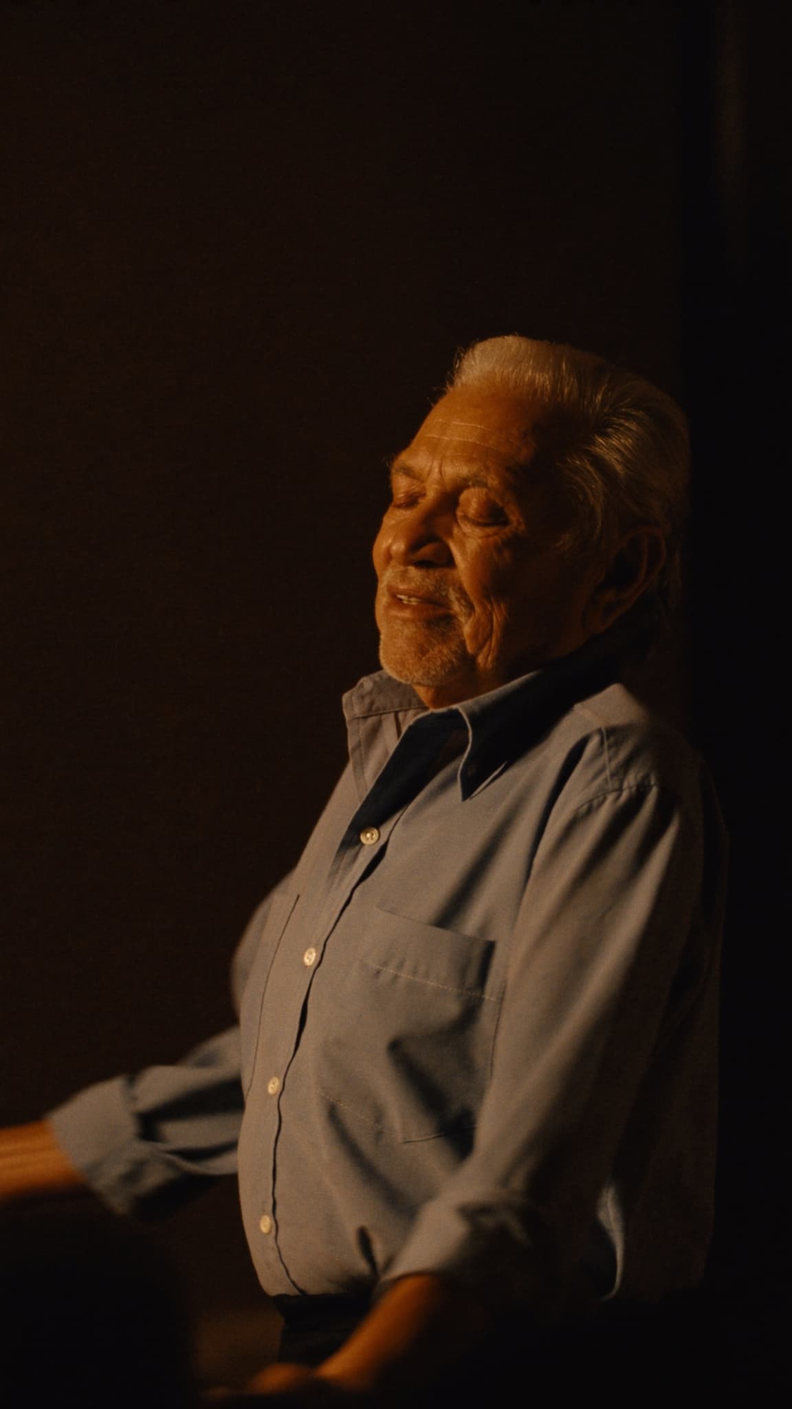 Abuelo latino bailando solo en su sala con luz dorada del atardecer