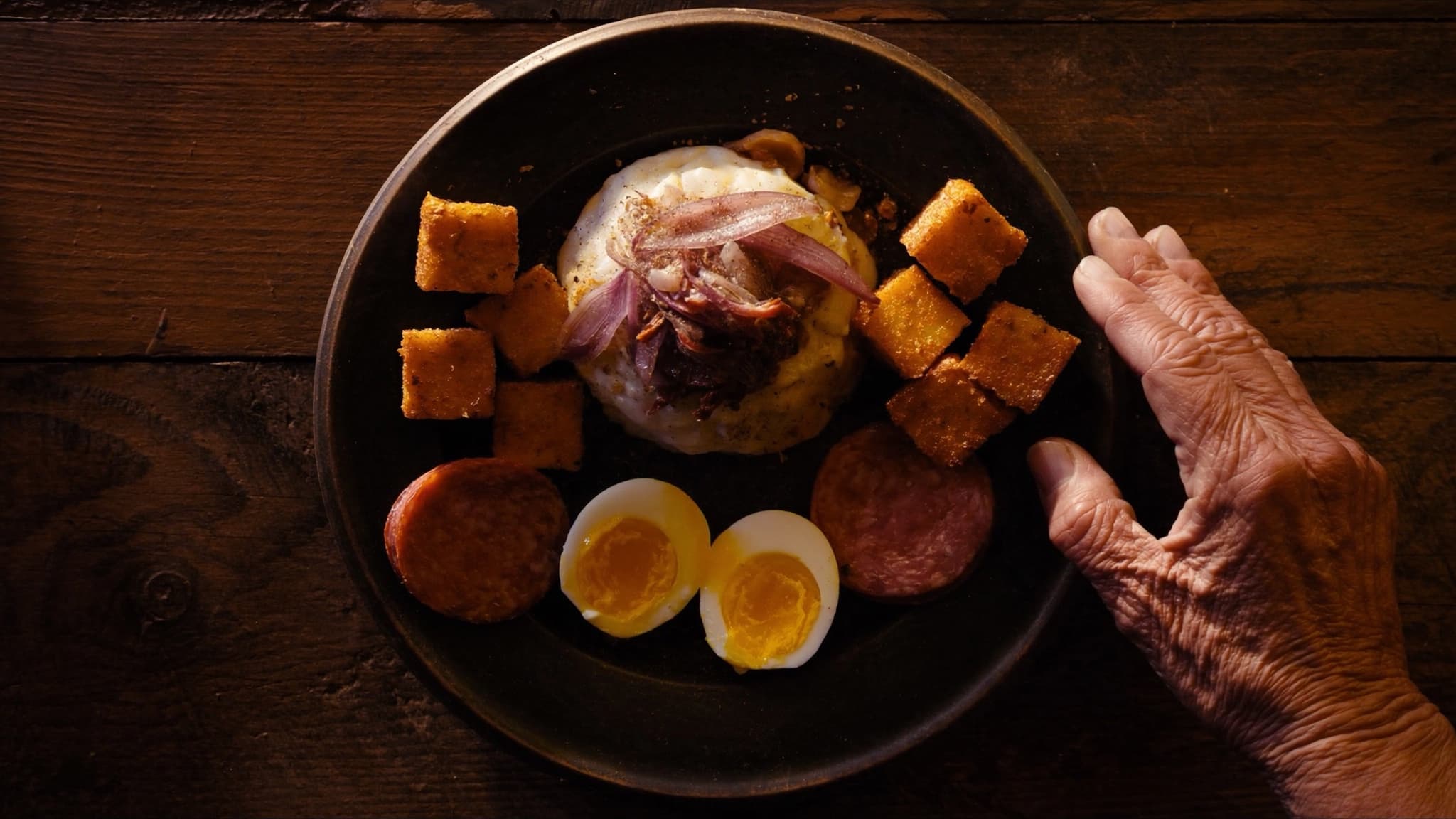 Plato de mangú dominicano con cebolla roja, huevos y queso frito sobre madera oscura